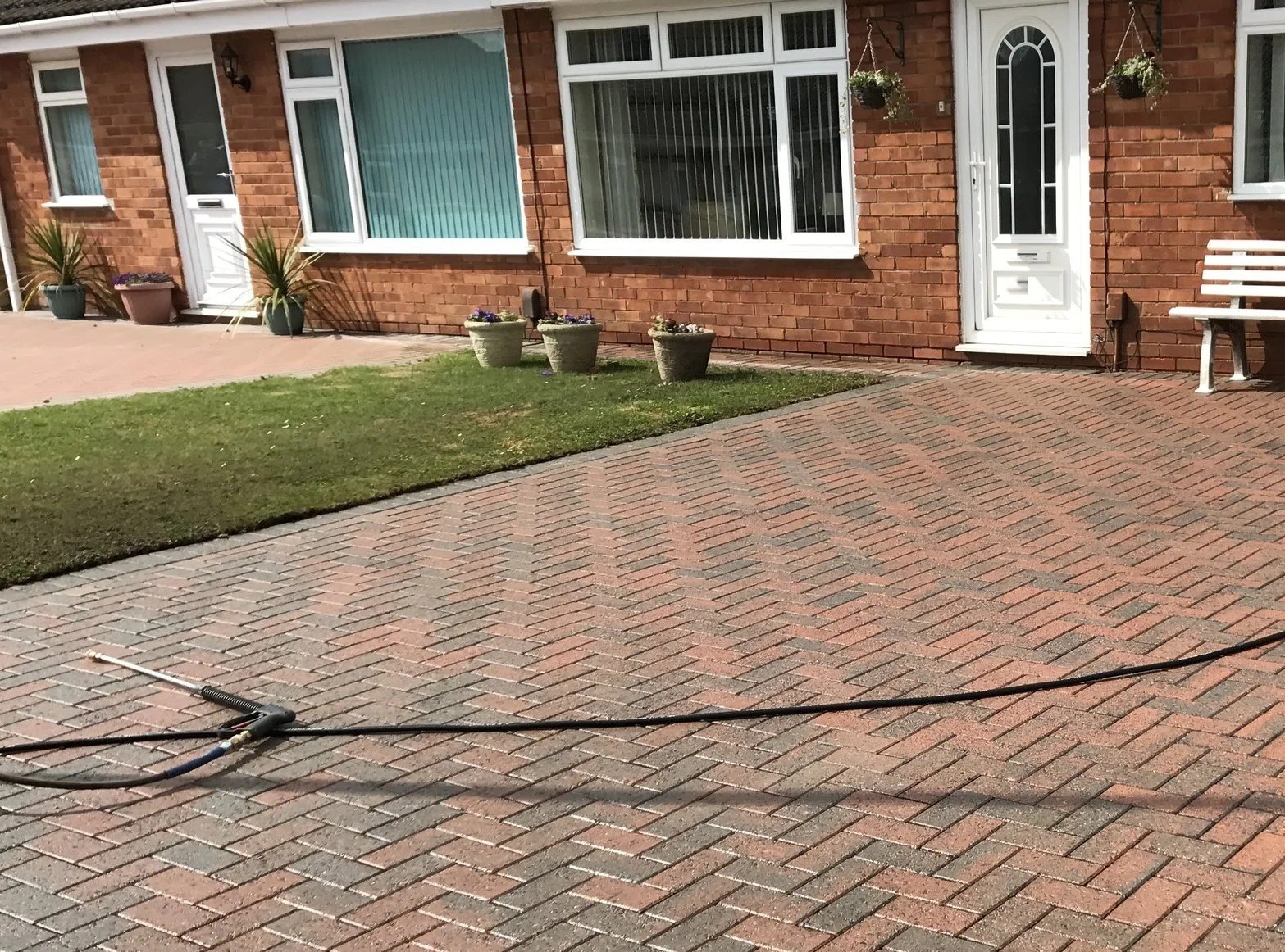 Block-paved driveway being power washed outside a brick bungalow